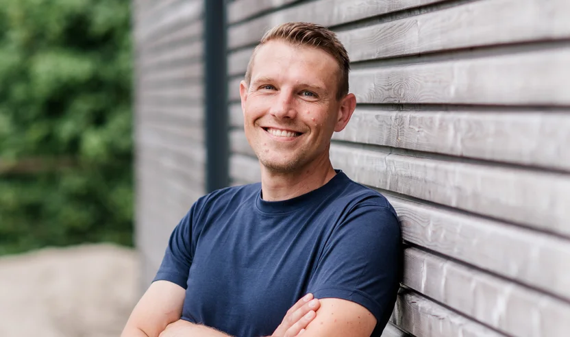 Alex Burgardt lehnt an einer Hauswand und lächelt freundlich in die Kamera.